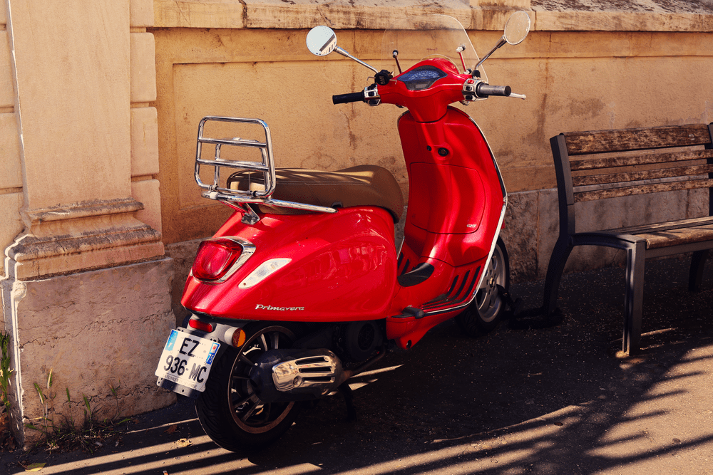A red Vespa scooter parked against a stone wall