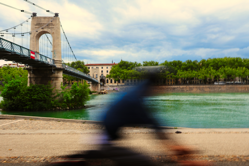 Motion-blurred cyclist passing a historic suspension bridge